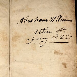 May include: A close-up of a handwritten inscription on a page of a book. The inscription reads "Abraham Williams, 1st July 1822".