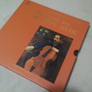 May include: A vintage orange box with gold lettering that reads "Prelude to Modern Music" and features a painting of a man playing a cello.