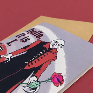 A2 illustrated adult greeting card featuring Nosferatu in a red and black coat, gothic lettering, and a red rose, with a kraft envelope. The words on the card read, "Hello, it is I, I've come to suck your..."