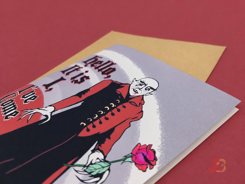 A2 illustrated adult greeting card featuring Nosferatu in a red and black coat, gothic lettering, and a red rose, with a kraft envelope. The words on the card read, "Hello, it is I, I've come to suck your..."