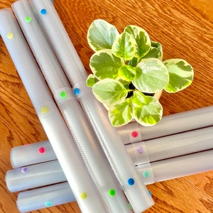 May include: A set of six clear silicone counter mats with colorful dots. The mats are rolled up and stacked on top of each other. The mats are designed to protect countertops from scratches and heat.