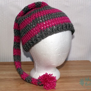 May include: A pink and gray striped crochet hat with a long tail and a pink pom pom. The hat is on a white styrofoam head.