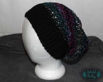Op de afbeelding: Een zwarte en veelkleurige gebreide beanie met een textuurontwerp. De beanie wordt getoond op een witte mannequinkop.