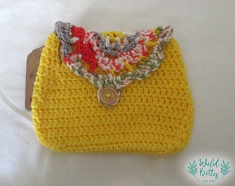 May include: A small yellow crocheted purse with a colourful crocheted flower design on the top flap. The purse has a single button closure.