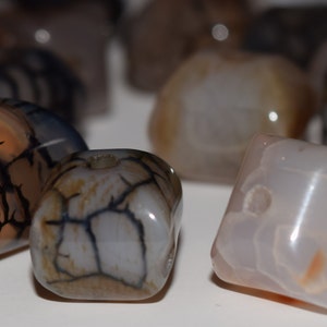 Könnte beinhalten: Eine Sammlung von Achatperlen in verschiedenen Formen und Größen. Die Perlen sind eine Mischung aus Weiß, Braun und Grau mit schwarzen Adern, die durch sie verlaufen.