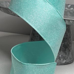Puede incluir: Un rollo de cinta ancha turquesa con acabado brillante. La cinta se muestra en espiral, mostrando su textura y color. Los bordes están cuidadosamente cosidos, agregando un aspecto acabado. Ideal para manualidades y envolver regalos.
