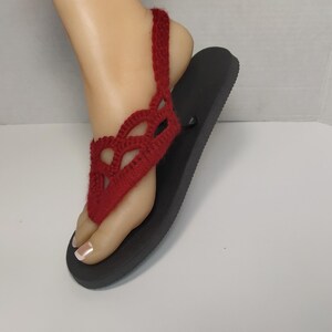 May include: Red crocheted sandals with a black sole. The sandals have a delicate, lacy design and a strap that goes around the ankle.
