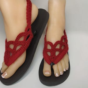 May include: Red crocheted sandals with a delicate, lacy design. The sandals have a black sole and an ankle strap.
