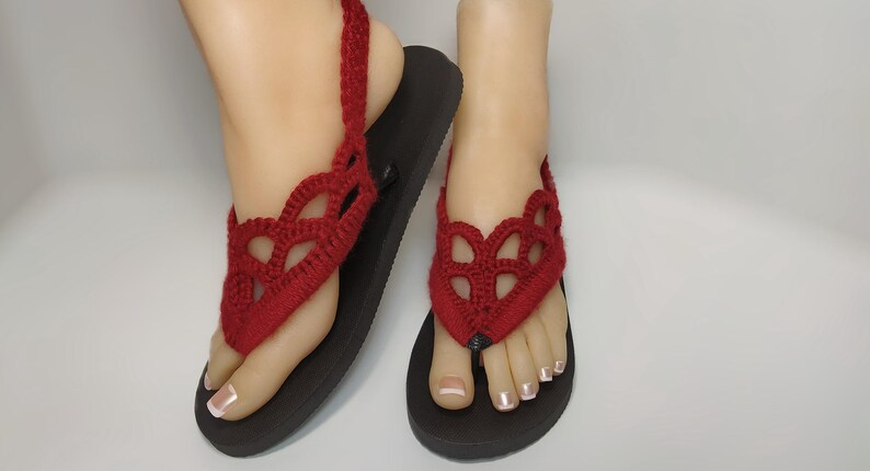 May include: Red crocheted sandals with a delicate, lacy design. The sandals have a black sole and an ankle strap.