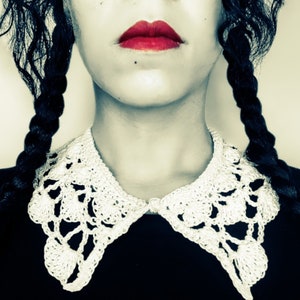 Peut inclure: Une femme aux cheveux noirs tressés porte un col en crochet blanc. Ses lèvres sont peintes d'un rouge vif.