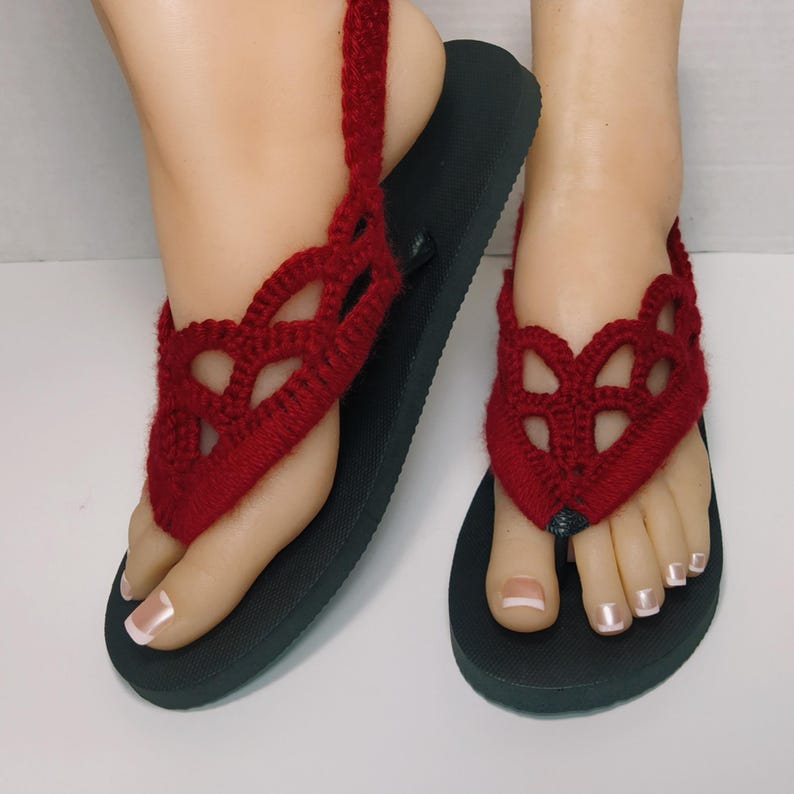 May include: A pair of red crocheted flip-flop sandals with a black sole.