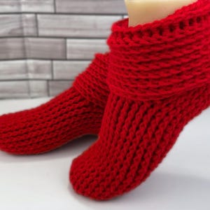 Könnte beinhalten: Ein Paar rote gestrickte Hausschuhe mit umgeklapptem Bündchen. Die Socken sind mit einem einfachen Stichmuster gearbeitet.