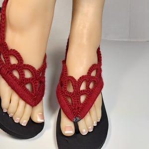 May include: Red crocheted flip-flop sandals with black soles. The sandals have a delicate, lacy design.