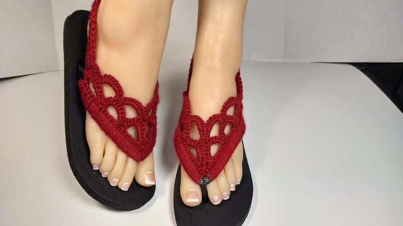 May include: Red crocheted flip-flop sandals with black soles. The sandals have a delicate, lacy design.