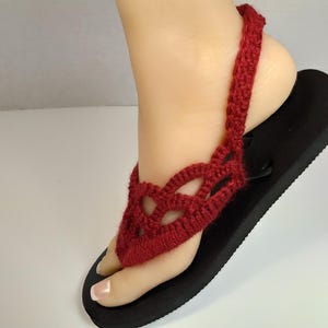 May include: Red crocheted sandals with a black sole. The sandals have a strap that goes around the ankle.