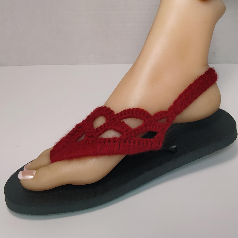 May include: Red crocheted sandals with a black sole. The sandals have a criss-cross design and an ankle strap.