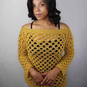Op de afbeelding: Mosterdgeel gehaakt off-the-shoulder top. De top heeft een uniek open weefpatroon en lange mouwen. Het kledingstuk is handgemaakt en biedt een comfortabele, stijlvolle uitstraling.