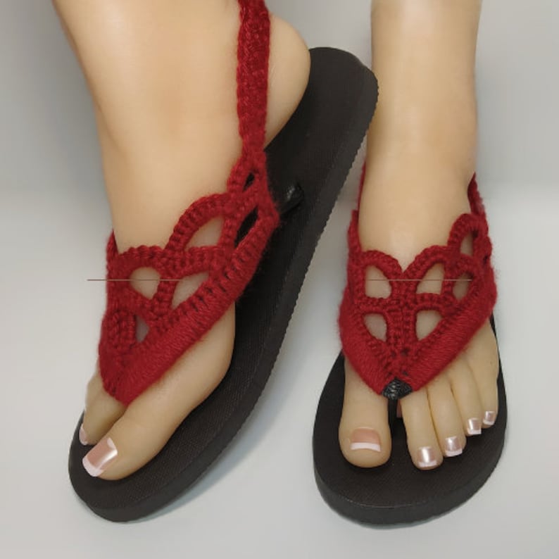 May include: A pair of red crocheted sandals with black flip-flop soles. The sandals have a delicate, lacy design and are perfect for summer.