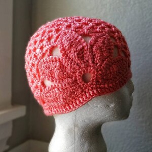 May include: A crocheted hat with a pink and white floral design. The hat has a lacy pattern and is made with a soft yarn.