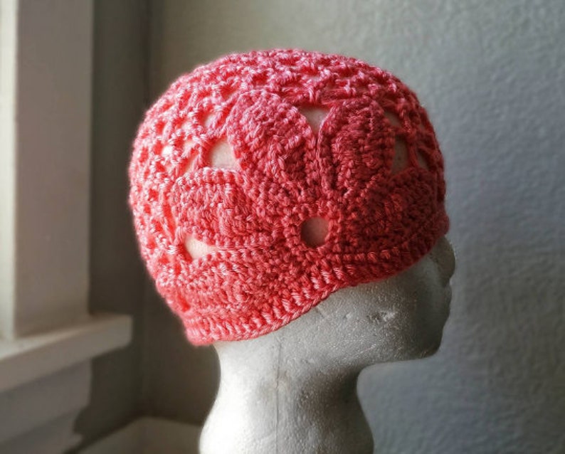 May include: A crocheted hat with a pink and white floral design. The hat has a lacy pattern and is made with a soft yarn.