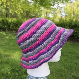 May include: A crocheted sun hat with wide brim in shades of pink, purple, and gray.