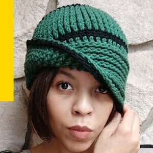 May include: A green and black crocheted cloche hat with a folded brim. The hat is worn by a person with dark hair and brown eyes.