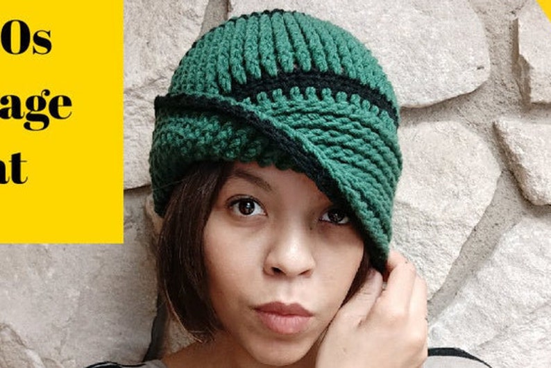 May include: A green and black crocheted cloche hat with a folded brim. The hat is worn by a person with dark hair and brown eyes.