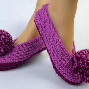 Peut inclure: Une paire de pantoufles tricotées dans des tons de violet, avec un gros pompon sur le bout de chaque pantoufle. Les pantoufles sont un article fait main et confortable, parfait pour l'intérieur.