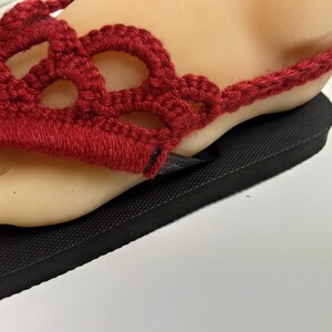 May include: Red crocheted sandals with a black sole. The sandals have a delicate, openwork design.