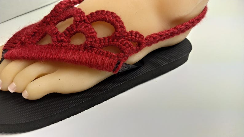 May include: Red crocheted sandals with a black sole. The sandals have a delicate, openwork design.