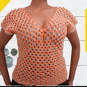 May include: A crocheted top with a V-neck and short sleeves. The top is made with a combination of peach and beige yarn, creating a striped pattern.