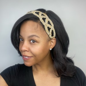 Puede incluir: Una diadema dorada y plateada con un diseño trenzado. La diadema la lleva puesta una persona con el pelo oscuro.