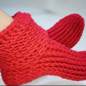 May include: Red knitted slipper socks with a ribbed texture. The socks are worn on a person's feet.