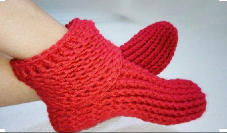 May include: Red knitted slipper socks with a ribbed texture. The socks are worn on a person's feet.