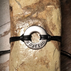 May include: A black leather bracelet with a silver metal ring that says "Spartan" on it.