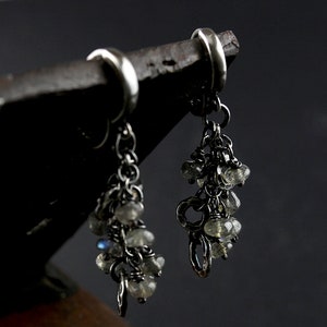 Peut inclure: Une paire de boucles d'oreilles pendantes en argent avec un groupe de pierres iris&eacute;es suspendues &agrave; chacune. Les boucles d'oreilles sont faites avec une cha&icirc;ne d&eacute;licate et ont un design simple de cerceau.