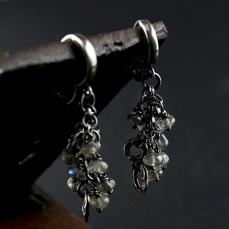 Peut inclure: Une paire de boucles d'oreilles pendantes en argent avec un groupe de pierres iris&eacute;es suspendues &agrave; chacune. Les boucles d'oreilles sont faites avec une cha&icirc;ne d&eacute;licate et ont un design simple de cerceau.