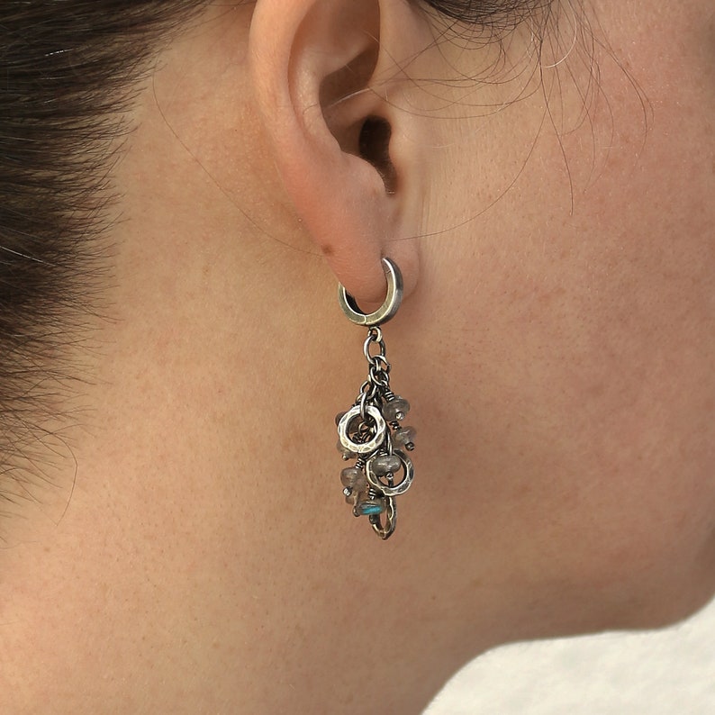 Peut inclure: Boucles d'oreilles cr&eacute;oles argent&eacute;es avec un charme suspendu compos&eacute; de plusieurs petits anneaux argent&eacute;s et de pierres grises et bleues.