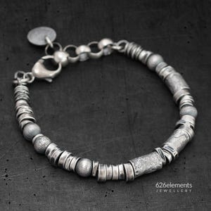 May include: A silver bracelet with a variety of textured beads and cylindrical elements. The bracelet features a lobster clasp and a small circular charm. The text "626elements JEWELLERY" is visible.