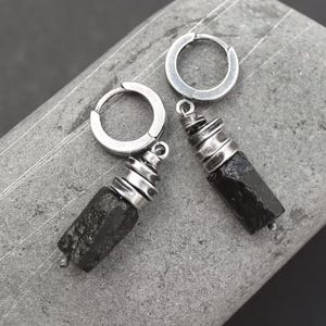 May include: A pair of silver hoop earrings with black stone pendants. The stones are rough and have a natural, organic look. The hoops are simple and sleek.