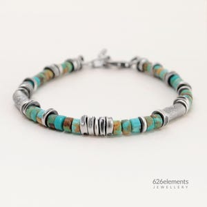 May include: A turquoise and silver beaded bracelet. The bracelet features small, round turquoise beads interspersed with silver-colored metal beads and cylindrical accents. The clasp is also silver-colored. The jewelry is displayed on a white background.