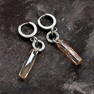 May include: A pair of silver hoop earrings with a dangling amber crystal charm. The hoops are simple and the crystals are faceted.