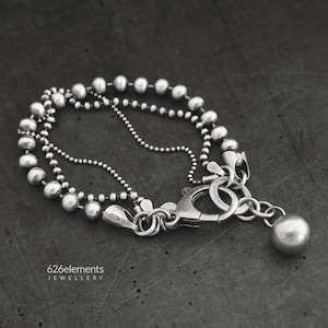 May include: A silver bracelet with a chain and a large silver bead. The bracelet has a clasp and a small silver charm.
