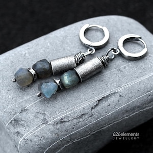 May include: A pair of drop earrings featuring silver-toned hoop closures attached to textured cylindrical metal beads and raw, faceted labradorite stones with blue and grey hues. The text 626elements JEWELLERY is visible in the bottom corner.