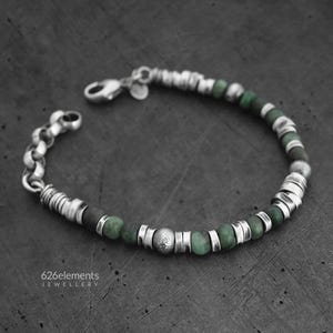 Op de afbeelding: Zilveren armband met groene en grijze kralen. De armband heeft een mix van ronde en cilindrische zilveren elementen, afgewisseld met donkergrijze en groene kralen. De sluiting is een karabijnhaak. De tekst "626elements JEWELLERY" is zichtbaar.