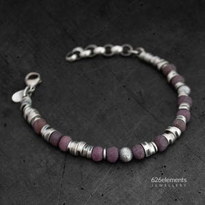 Peut inclure: Un bracelet en argent avec des perles violettes et un charme en argent. Le bracelet est sur un fond gris foncé. 626elements JEWELLERY.