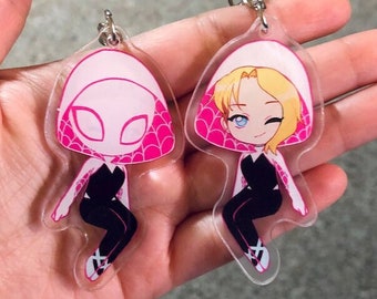 May include: Two clear acrylic keychains featuring a cartoon character wearing a pink and white hooded costume. The character is in a sitting pose with one leg crossed over the other. The character on the left has a white face with black eyes, while the character on the right has a blonde ponytail and blue eyes.