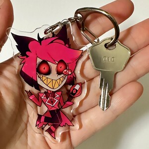 May include: A red and black cartoon character keychain with a large grin and red eyes. The keychain is attached to a silver key ring and a silver key with the number "010" on it.