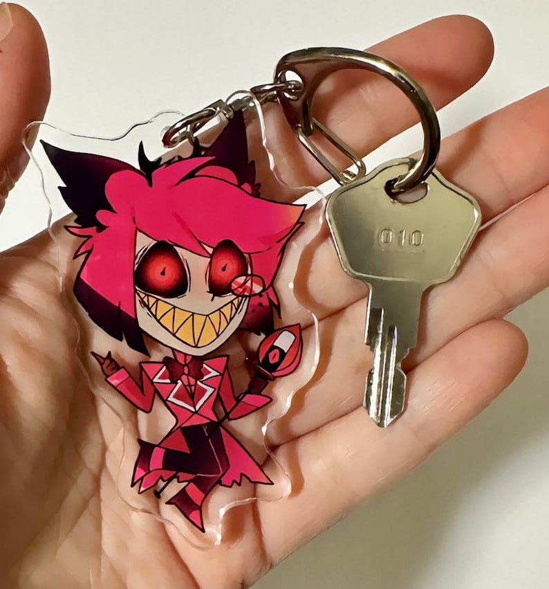 May include: A red and black cartoon character keychain with a large grin and red eyes. The keychain is attached to a silver key ring and a silver key with the number "010" on it.