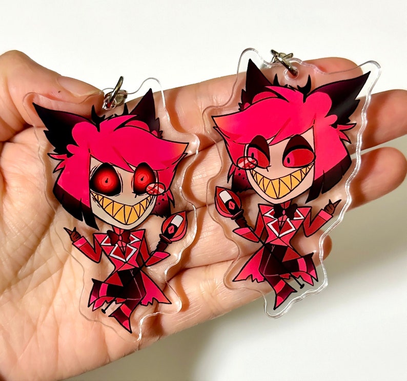 May include: Two red and black cartoon character keychains with a devilish grin. The characters have red hair, black eyes, and are wearing a red suit with a white collar and bow tie.